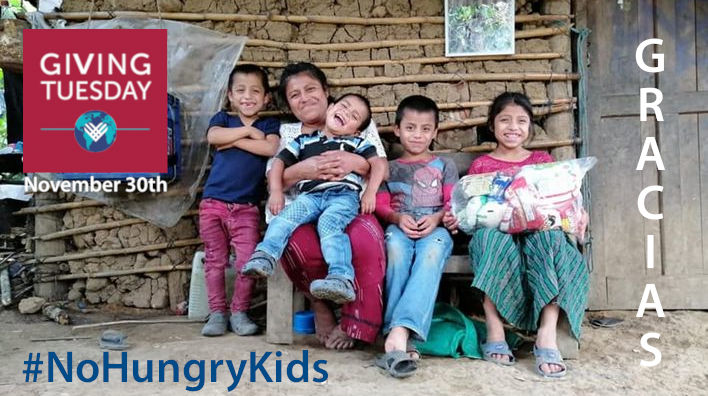 A family of a mother and four children sitting in front of a mud stick wall with huge smiles with the daughter holding a large food hamper. Text says Gracias and includes the Giving Tuesday Logo and the No Hungry Kids hashtag